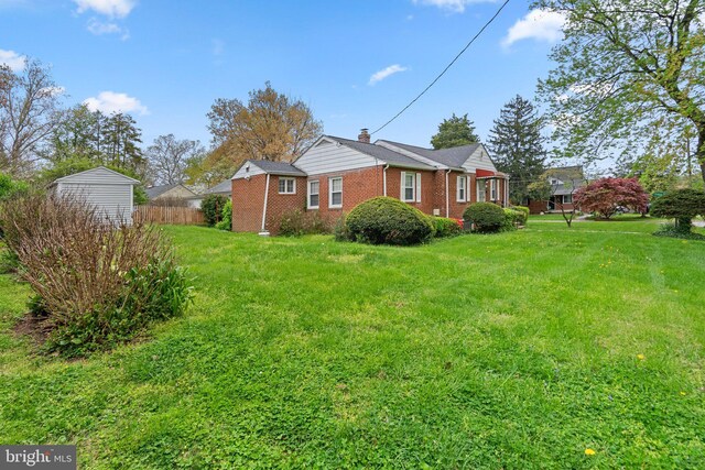 view of side of home with a chimney, brick siding, fence, and a yard