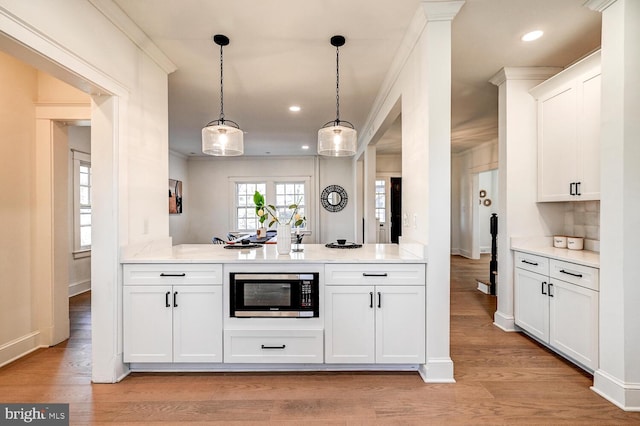 kitchen featuring stainless steel microwave, decorative light fixtures, white cabinets, and light countertops