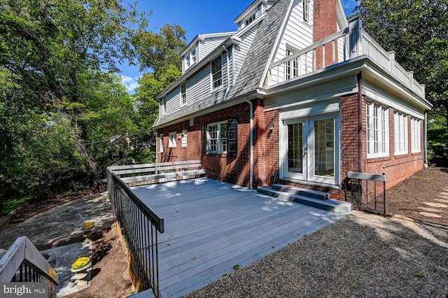 rear view of property with brick siding, french doors, a chimney, and a balcony