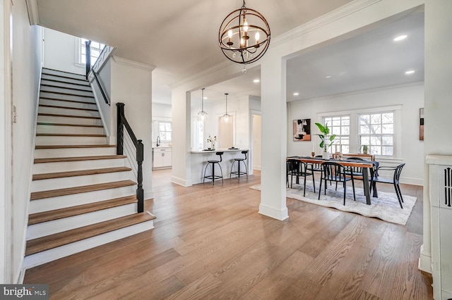 entryway featuring crown molding, a chandelier, wood finished floors, and stairs