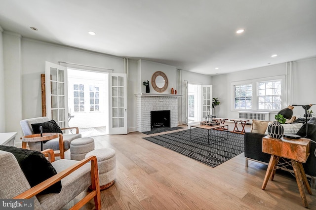 living room featuring radiator, a fireplace, recessed lighting, wood finished floors, and french doors