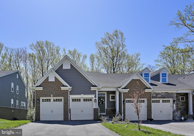 craftsman-style home featuring brick siding, an attached garage, driveway, and stone siding