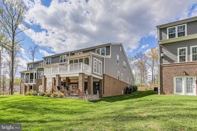 rear view of property featuring a lawn, a wooden deck, brick siding, and a patio area