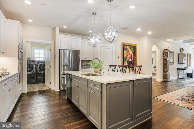kitchen featuring washer and clothes dryer, visible vents, gray cabinets, a sink, and arched walkways
