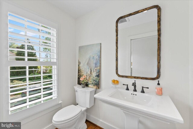 half bathroom with toilet, baseboards, a wealth of natural light, and wood finished floors
