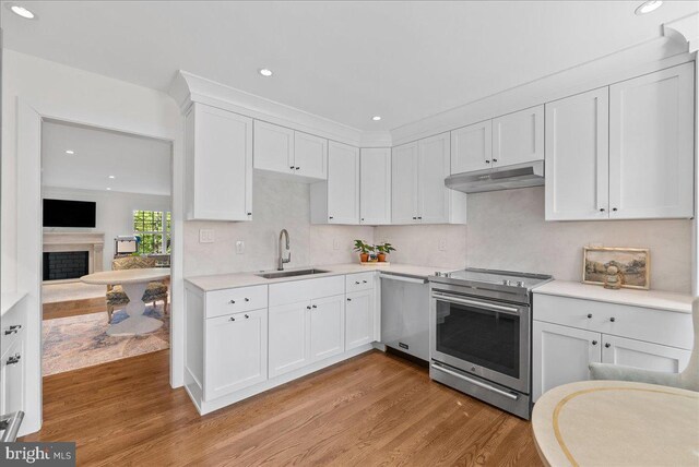 kitchen featuring light wood-type flooring, a sink, white cabinets, under cabinet range hood, and stainless steel appliances