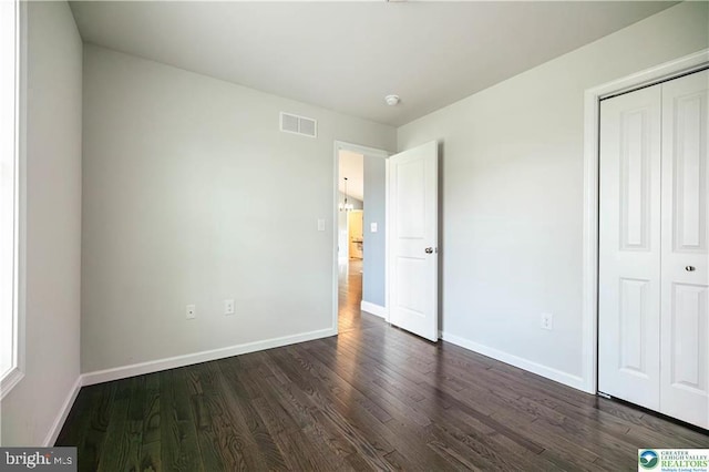 unfurnished bedroom featuring a closet, dark wood-style flooring, baseboards, and visible vents