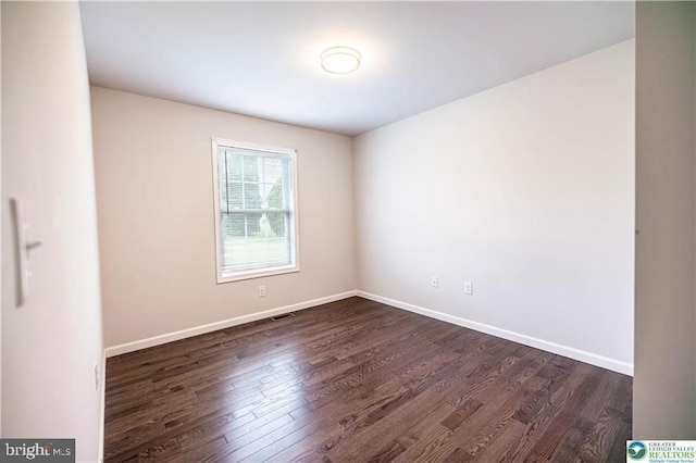 spare room featuring dark wood-style flooring, visible vents, and baseboards