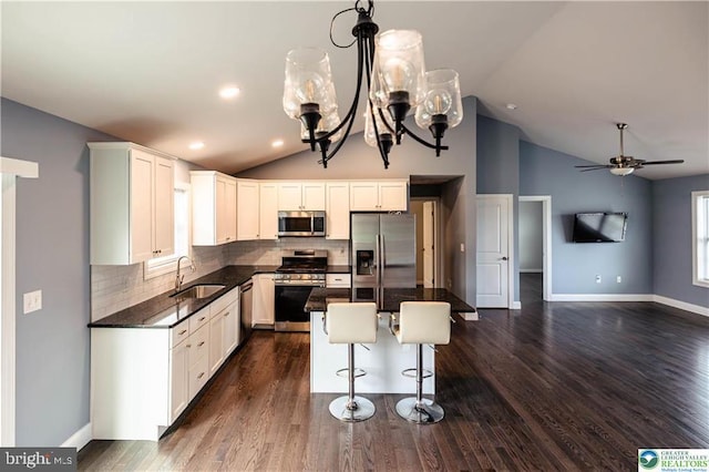 kitchen featuring appliances with stainless steel finishes, vaulted ceiling, a center island, decorative backsplash, and a sink