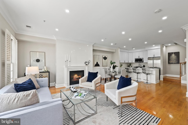 living area featuring light wood finished floors, visible vents, recessed lighting, and ornamental molding