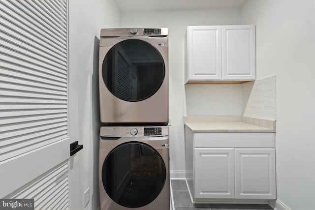 washroom featuring stacked washer / drying machine, tile patterned floors, baseboards, and cabinet space