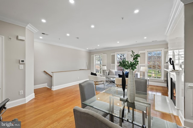 dining room with baseboards, recessed lighting, light wood-style floors, a warm lit fireplace, and crown molding