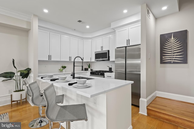 kitchen with a breakfast bar, stainless steel appliances, light countertops, white cabinetry, and visible vents