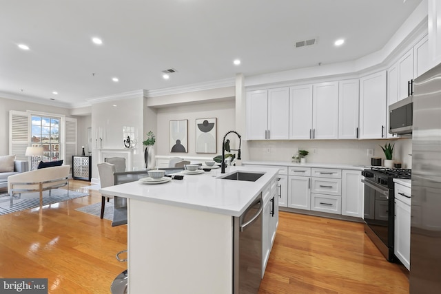 kitchen with stainless steel appliances, a sink, visible vents, crown molding, and an island with sink