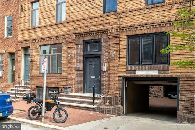 doorway to property featuring an attached garage, brick siding, and concrete driveway