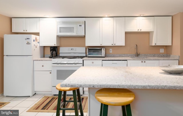 kitchen with a sink, a breakfast bar area, white cabinets, and white appliances