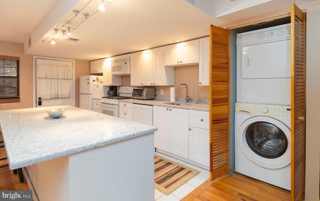 kitchen featuring stacked washer / dryer, white appliances, white cabinetry, light stone counters, and a sink