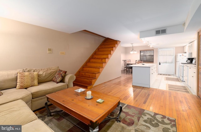 living room with visible vents, light wood finished floors, and stairs