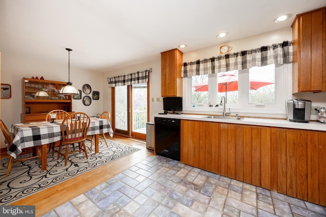 kitchen featuring brown cabinetry, light countertops, a sink, and black dishwasher