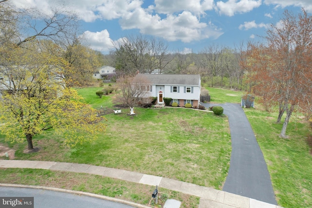 raised ranch with aphalt driveway, a wooded view, and a front yard