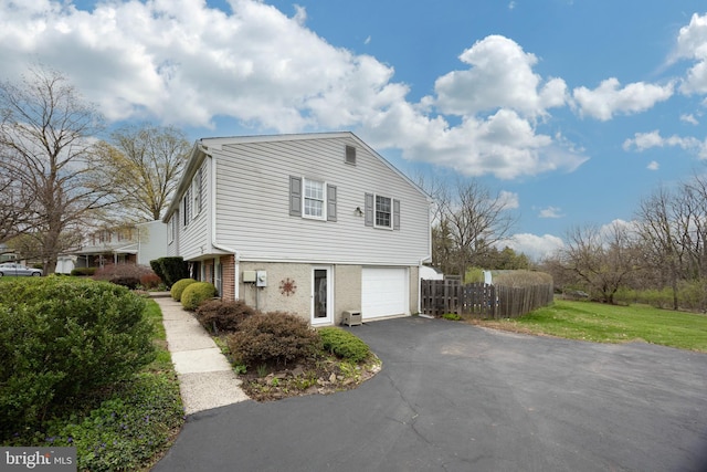 view of property exterior with a lawn, an attached garage, fence, and driveway
