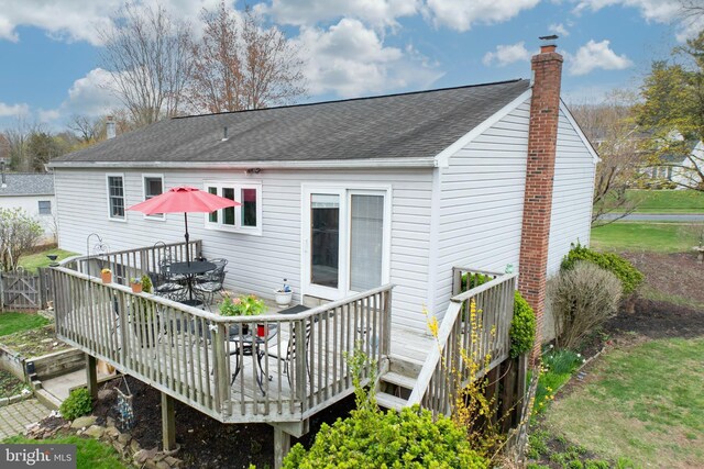 rear view of property featuring a chimney, roof with shingles, a deck, and outdoor dining area