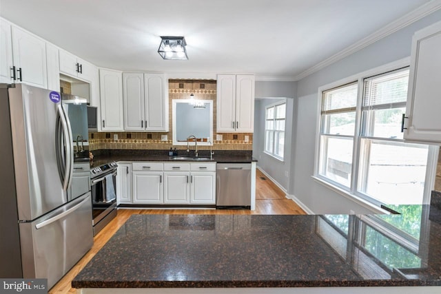 kitchen with white cabinets, a sink, light wood finished floors, stainless steel appliances, and decorative backsplash