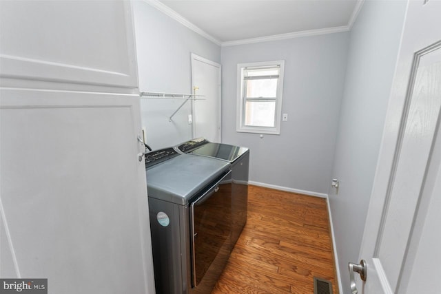 laundry room with washing machine and clothes dryer, laundry area, wood finished floors, visible vents, and ornamental molding