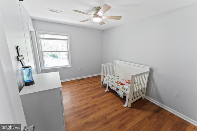 bedroom with baseboards, a crib, wood finished floors, and visible vents