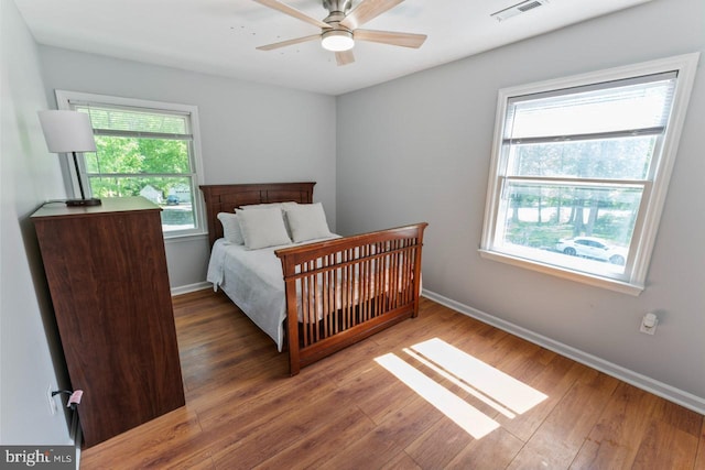 bedroom featuring visible vents, baseboards, wood finished floors, and multiple windows