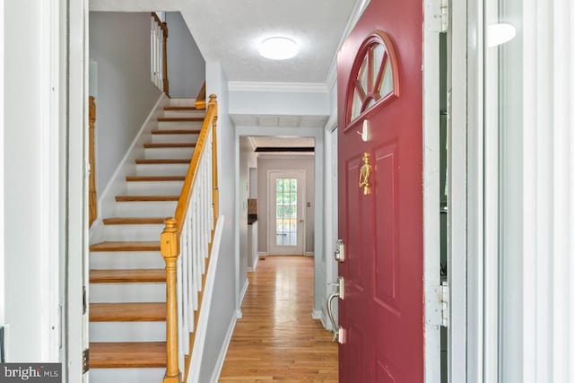 foyer featuring a textured ceiling, light wood-type flooring, baseboards, ornamental molding, and stairs