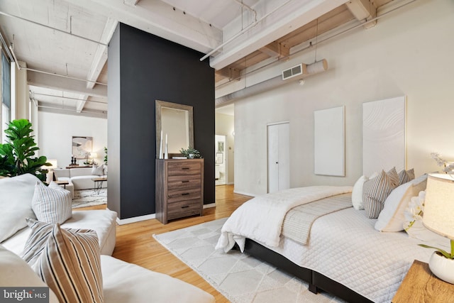 bedroom with wood finished floors, a towering ceiling, beam ceiling, and visible vents