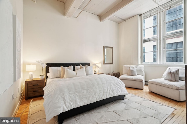 bedroom with baseboard heating, multiple windows, beamed ceiling, and wood finished floors