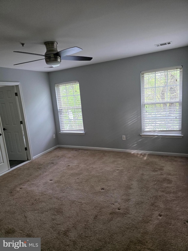 carpeted empty room with visible vents, baseboards, and ceiling fan