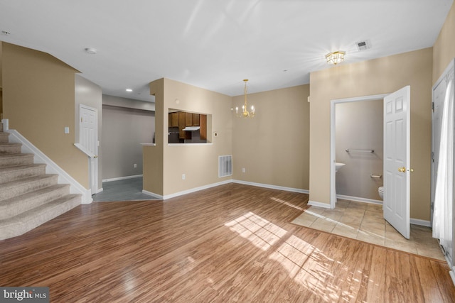 unfurnished living room with light wood-style flooring, a chandelier, visible vents, and stairs