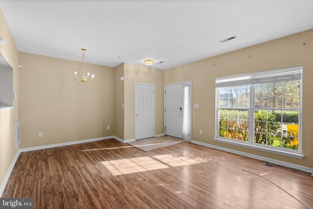 unfurnished living room featuring visible vents, baseboards, an inviting chandelier, and wood finished floors