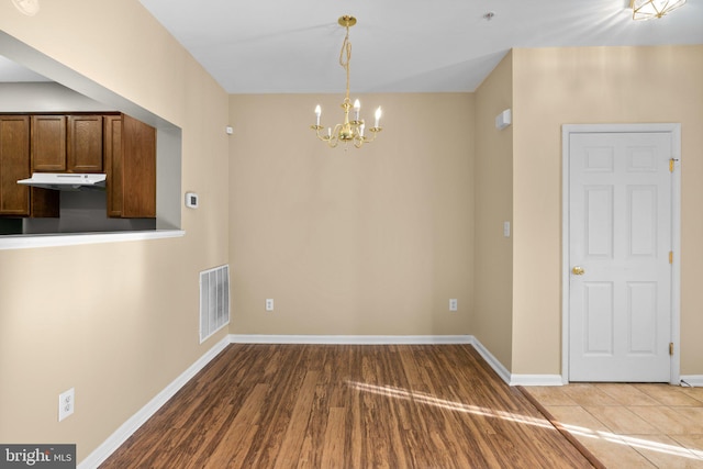 unfurnished dining area featuring visible vents, baseboards, a chandelier, and wood finished floors