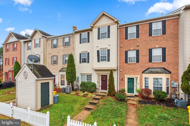 townhome / multi-family property with an outbuilding, a shed, central air condition unit, a front yard, and fence