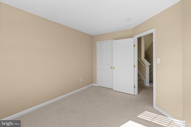 unfurnished bedroom with light carpet, baseboards, and a closet