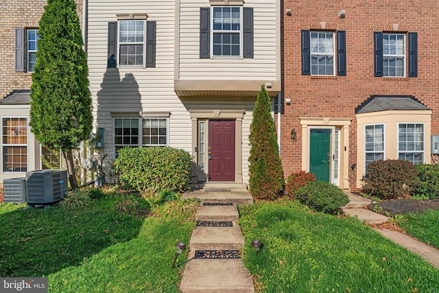 townhome / multi-family property featuring central air condition unit, a front lawn, and brick siding