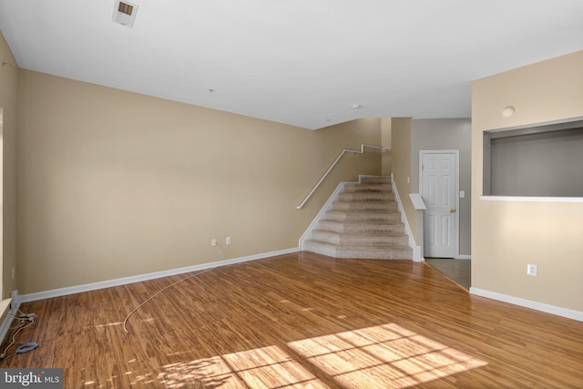 unfurnished living room with stairway, visible vents, baseboards, and wood finished floors