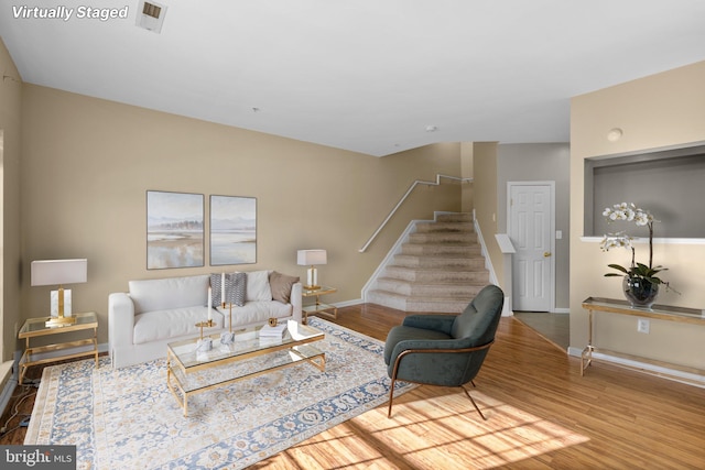 living room featuring stairway, visible vents, baseboards, and wood finished floors