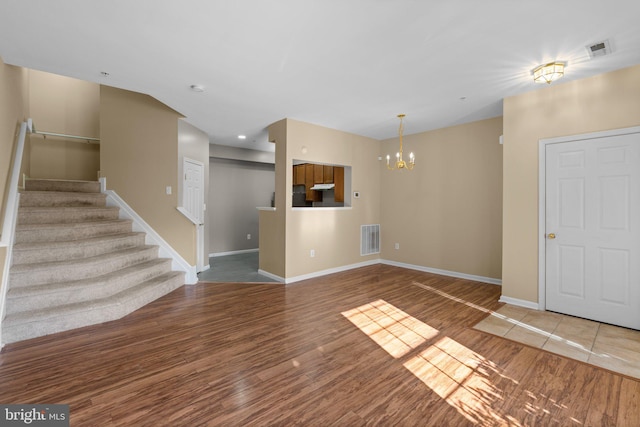 unfurnished living room featuring visible vents, stairway, an inviting chandelier, and wood finished floors