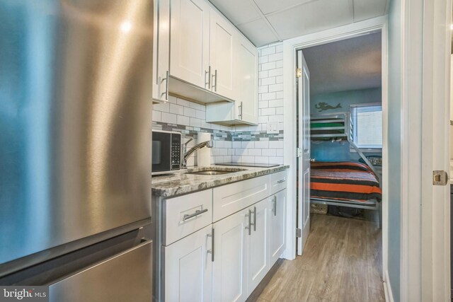 kitchen with light wood finished floors, freestanding refrigerator, white cabinetry, decorative backsplash, and light stone countertops