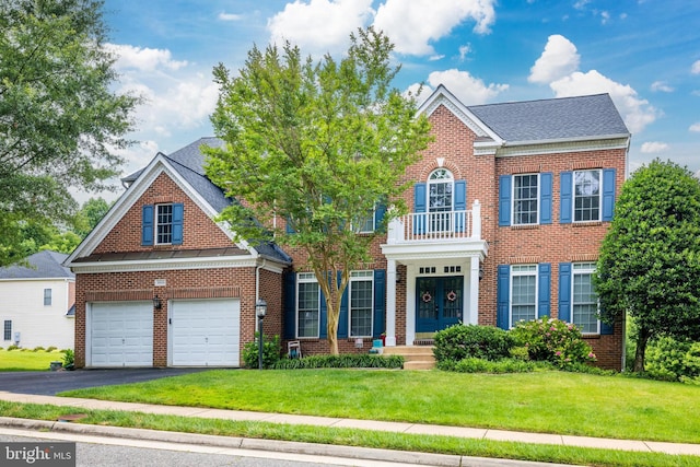 colonial-style house with a balcony, french doors, aphalt driveway, brick siding, and a front yard