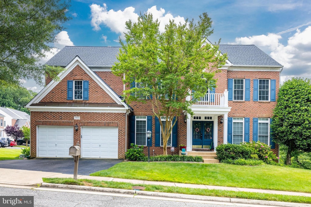 view of front of property with a balcony, driveway, french doors, a front lawn, and brick siding