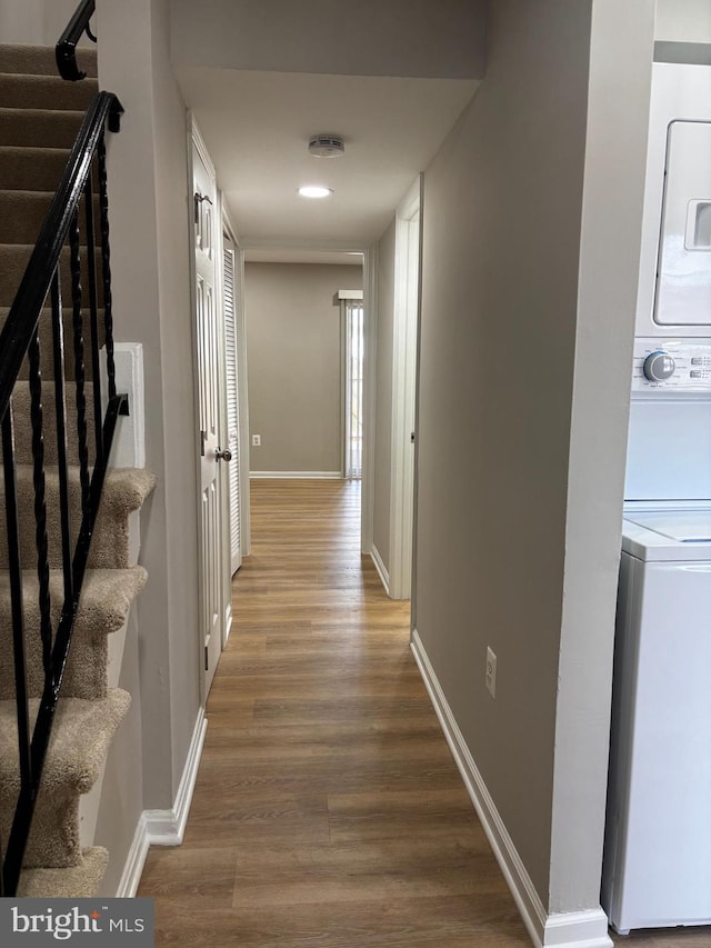 corridor featuring stacked washer and dryer, baseboards, wood finished floors, and stairway