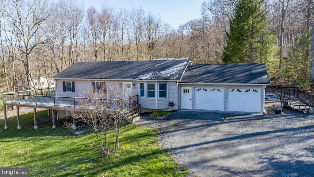 single story home featuring a garage, a wooden deck, a front yard, a forest view, and driveway