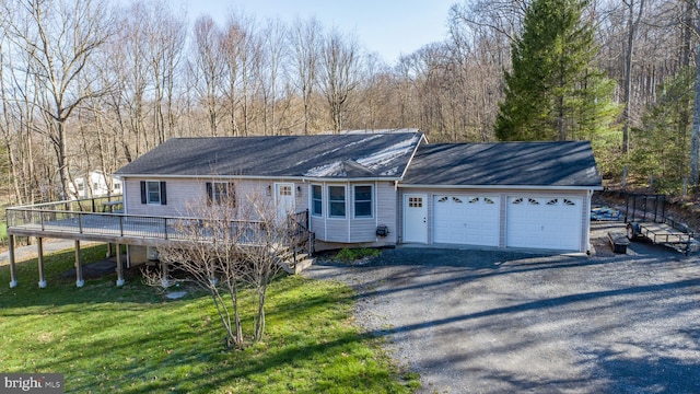 single story home featuring a garage, a wooden deck, a front yard, a forest view, and driveway