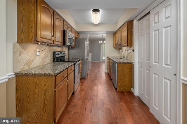 kitchen with a sink, appliances with stainless steel finishes, brown cabinets, and dark wood-style floors